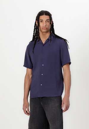 Chemise bleu marine à manches courtes en tissu léger, avec un devant à boutons, un col décontracté et un éclat subtil. Associée à un jean noir.
