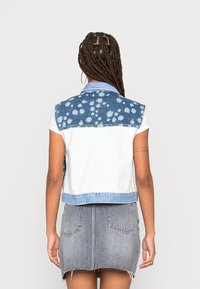 Jeansowa kamizelka z niebieskim wzorem kwiatowym na plecach, białym przodem i kołnierzykiem. W połączeniu z szarą jeansową spódnicą z postrzępionym dołem.