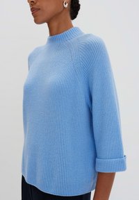 Himmelblaues, geripptes Strickoberteil mit hohem Kragen, Dreiviertelärmeln und aufgerollten Bündchen. Weiche Textur und entspannter Schnitt.