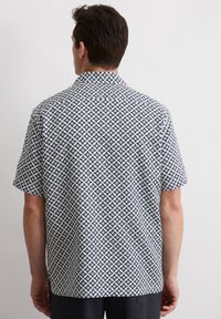 Camicetta a maniche corte in tessuto leggero con un motivo geometrico a stelle in navy e bianco. Colletto classico con una vestibilità rilassata.