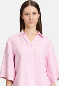 Rosa Leinen-Hemd mit Knopfleiste, V-Ausschnitt, kurzen Ärmeln und subtilem Texturmuster. Verfügt über eine Reihe von Knöpfen auf der Vorderseite und einen klassischen Kragen.