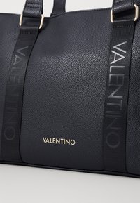 Černá kožená taška přes rameno s texturou kůže, zlatým logem a tónovými látkovými popruhy s raženým nápisem "VALENTINO".
