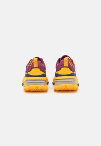 Multicolored athletic shoes featuring a purple upper, yellow accents, and a textured rubber sole with deep grooves for traction.