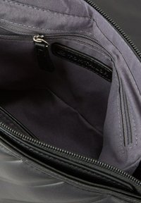 Interior de una bolsa de tela negra con una textura suave, que presenta un bolsillo con cremallera y un parche con el logo. El forro es de un gris oscuro contrastante.