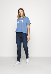 Mėlyna trumpa marškinė su baltu "LEVI'S" logotipu, derinami su tamsiais džinsiniais siaurais džinsais ir baltais sportbačiais. Lygus audinys, laisvas kirpimas.
