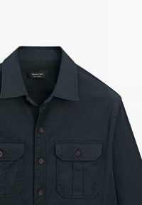 Chemise bleu marine foncé boutonnée avec deux poches à rabat boutonnées à l’avant et un col classique, étiquette Massimo Dutti.