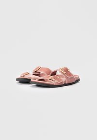 Sandali slide in velluto rosa con due fibbie dorate regolabili e suole piatte nere su uno sfondo bianco.