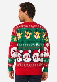 Raudonas Kalėdų megztinis su elniais, Kalėdų Senelio veidais ir geltonomis žvaigždėmis. Megztas raštas su žaliais ir baltais akcentais, ilgomis rankovėmis, faktūruota medžiaga.