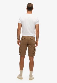 Bruine cargoshorts met zijzakken, gecombineerd met een wit T-shirt en beige schoenen. Heeft een ontspannen pasvorm en een knielange snit.