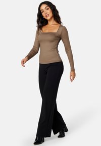 Braun gestreiftes Langarmoberteil mit quadratischem Ausschnitt, kombiniert mit schwarzen Schlaghosen und schwarzen stiefeletten mit Absatz. Glatte Textur über die gesamte Fläche.