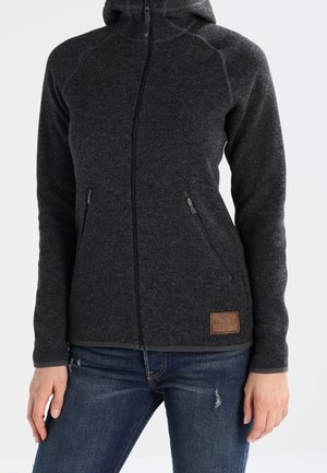 Donkergrijze fleecevest met rits en capuchon, twee zijzakken met rits, gedragen met blauwe spijkerbroek.