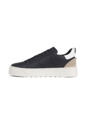 Scarpa da ginnastica nera low-top con suola bianca, linguetta del tallone bianca e accento in suede beige sulla parte posteriore, vista dal lato esterno.