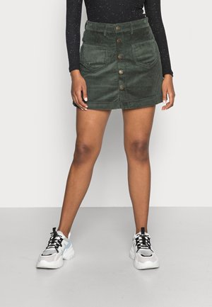 Grøn mini-nederdel i fløjl med forlommer foran, knaplukning og en tætsiddende talje, stylet med chunky hvide og sorte sneakers.