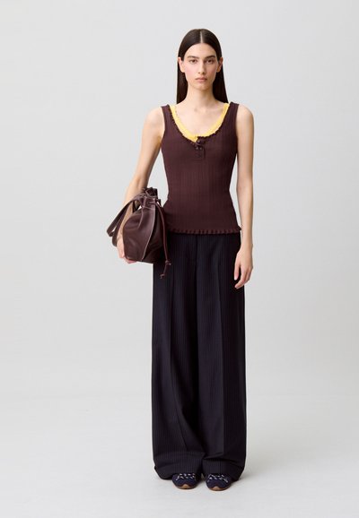 Top a coste marrone scuro con rifiniture e bottoni gialli, abbinato a pantaloni neri a gamba larga plissettati. Accessoriato con una borsa secchiello marrone.