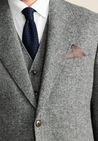 Gray wool blazer with a textured finish, featuring two buttons, a blue knitted tie, and a brown pocket square in a pointed fold.