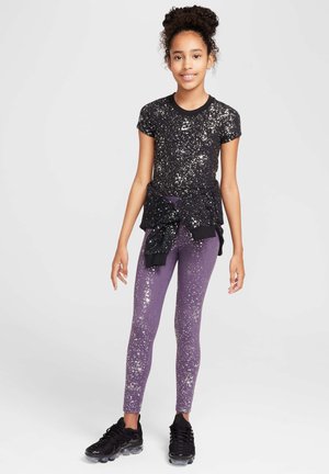 Camiseta negra con manchas plateadas, combinada con leggins morados con un patrón similar y zapatillas negras. Suéter negro atado a la cintura.