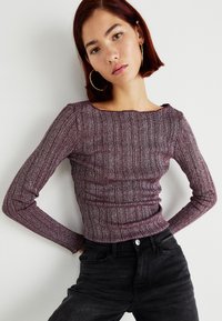 Maroon ribbed long-sleeve top with a scoop neckline, featuring a textured fabric and fitted silhouette, paired with black high-waisted jeans.