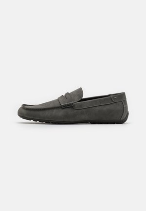 Mocassin en daim gris avec un bout arrondi, des détails cousus et une semelle en caoutchouc plate. La chaussure a une texture lisse et une bande avant décorative.