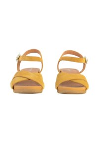 Sandali in suede giallo con design a strappo incrociato, cinturino alla caviglia regolabile e suola in gomma piatta. Texture liscia con dettagli minimi.