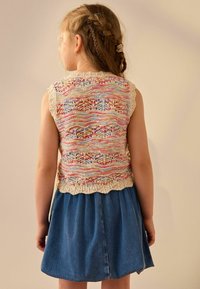 Top senza maniche lavorato a maglia con motivo multicolore e fondo scallop, abbinato a una gonna di jeans con pieghe e forma svasata.