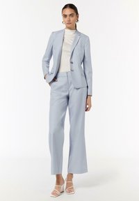 Helles blaues maßgeschneidertes Anzug mit einem einreihigen Blazer und weit geschnittenen Hosen. Weißes, figurbetontes Oberteil darunter, kombiniert mit weißen Riemchenschuhen.