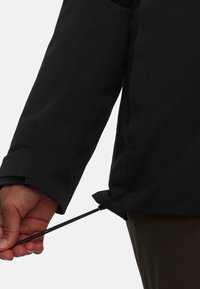 Schwarze wasserdichte Jacke mit verstellbarem Kordelzug am Saum, der gerade festgezogen wird. Glatte Textur, Mittelarmärmel und taillierte Passform.