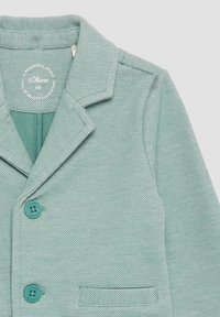 Pistaziengrüner Blazer mit strukturierter Oberfläche, mit Reverskragen, zwei türkisfarbenen Knöpfen und einer einzelnen Brusttasche. Leichter Stoff.