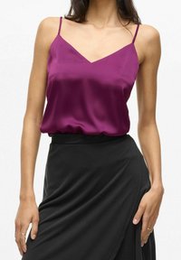 Camisole en satin magenta vif avec des bretelles fines réglables, présentant un décolleté en V et une coupe décontractée, associée à une jupe noire.