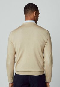 Lichtbeige sweater met lange mouwen en een ronde halslijn. Kenmerkt zich door ribgebreide mouwen en zoom, gestructureerde elleboogpatches en een gladde afwerking.