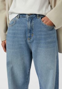 Jasnoniebieskie jeansy z denimu z wysokim stanem, prostymi nogawkami i wyblakłym wykończeniem. Charakterystyczne przeszycia kontrastowe i przednie kieszenie.