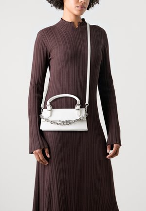 Weiße Handtasche mit strukturiertem Design, Kettenakzenten und kurzen Griffen, quer über einem langen, braunen, gerippten Kleid getragen.