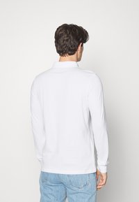 Vit långärmad pikétröja med krage, tillverkad av bomullstyg. Har en rak skärning och ribbade ärmslut. Bärs med ljusblå denimjeans.