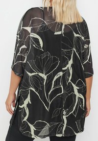 Kimono trasparente nero con motivi floreali verde chiaro, vestibilità larghi, maniche corte e spacchi laterali per facilitare il movimento.