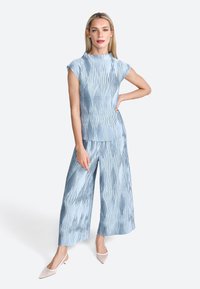 Completo in due pezzi di colore blu chiaro realizzato in tessuto testurizzato, con una maglietta a maniche corte e pantaloni a gamba larga con righe verticali.