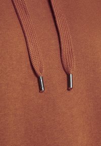 Sudadera con capucha en color óxido, con cordones trenzados con puntas de metal plateado y una tela suave y texturizada.