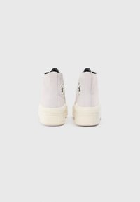 Adidași înalți din suede gri deschis, cu o talpă din cauciuc alb. Prezintă un logo circular pe călcâi și un panou lateral texturat.