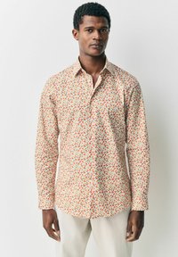 Camisa de manga larga hecha de tejido ligero, con un patrón de hojas multicolores sobre un fondo claro y un diseño de cuello clásico.