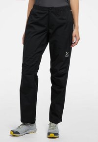 Svarta vattentäta vandringsbyxor med elastisk midja, avsmalnande ben och en reflekterande logotyp på sidan. Lättvikts, slitstarkt tyg.