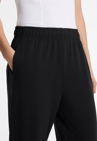 Black joggers made of soft fabric with an elastic waistband, side pockets, and a smooth texture. Designed for casual wear.