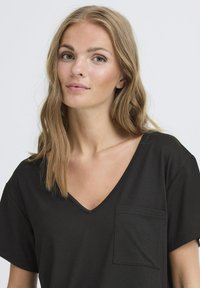 Tricou negru cu mânecă scurtă și decolteu în V, realizat din bumbac moale, având o mică buzunar pe piept și croi lejer pentru confort.