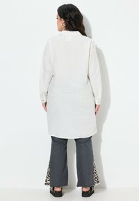 Pitkähihainen valkoinen paita, jossa on kauluspaita. Ominaisuudet: yksivärinen design, nappihihat ja rento leikkaus. Yhdistetty tummiin leveälahkeisiin farkkuihin, eläinkuosilla varustettuja yksityiskohtia.