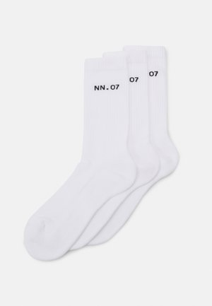 Trois paires de chaussettes en coton blanc avec une texture côtelée, arborant le texte noir "NN. 07" sur le côté. Design standard à mi-mollet.
