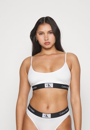 Witte katoenen bralette met dunne bandjes en een zwarte band met het "Calvin Klein" logo, gecombineerd met bijpassende witte bikini-achtige slipjes.