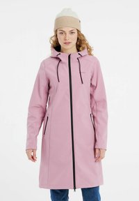 Ružový vodoodpudivý kabát s kapucňou, dlhými rukávmi, čiernym zipsom a prednými vreckami. Model má na sebe béžovú pletenú čiapku.