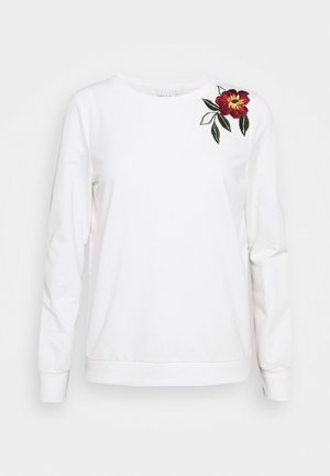 Biała bluza z długim rękawem o okrągłym dekolcie, z czerwonym haftem kwiatowym i zielonymi liśćmi na prawym ramieniu.
