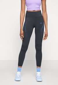 Leggings noirs taille haute avec accents latéraux bleus, en tissu extensible, associés à des chaussures de sport bleu clair et des chaussettes rayées.