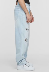 Light blue denim jeans with a loose fit, featuring two large rips and a straight leg design, worn with white sneakers.