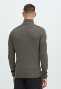 Gestrickter Pullover in dunkelolivgrün mit hohem Rippkragen, langen Ärmeln und geripptem Saum. Das Material wirkt weich mit einer strukturierten Oberfläche.
