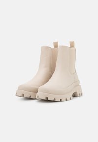 Bottines beiges en cuir lisse avec des panneaux latéraux élastiques et des tirettes. Semelles épaisses et robustes avec des cramponnages profonds pour une meilleure traction.