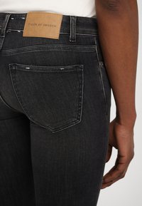 Svarte denimjeans har et klassisk design med en middels høy midje og et lærmerke merket "TIGER OF SWEDEN." Teksturen er glatt med subtil falming.